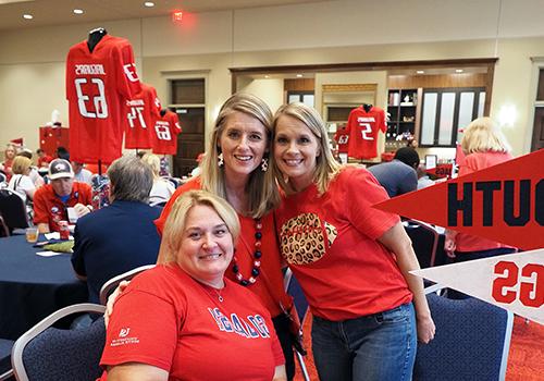 Three alumni members at an event at the MacQueen Center wearing their Jag Gear.