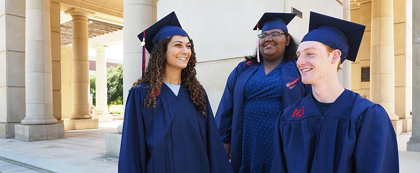 Three USA graduates in their cap and gowns smiling.